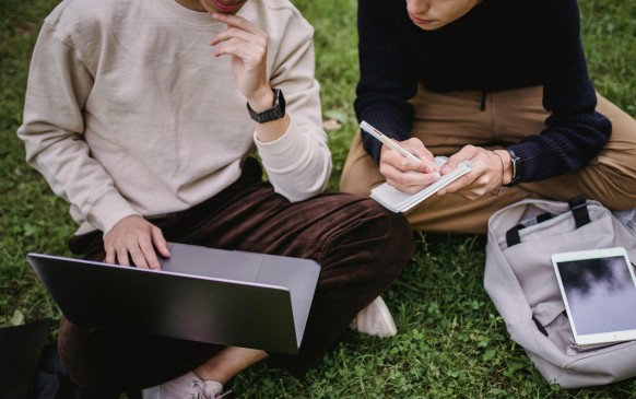 Crop ethnic male students using laptop while studying in park